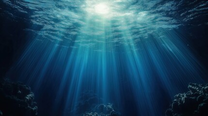 Sunlight beams pierce deep ocean water. Water is dark blue and transparent. Sun rays illuminate underwater rocks. Ocean depths are calm and tranquil. This serene underwater scene is beautiful.