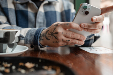Woman using smartphone at cafe table showing hand tattoos
