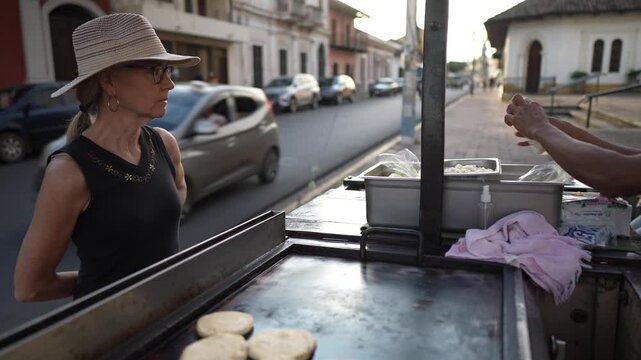 A mature woman tourist engages with a street food vendor in Granada, Nicaragua, as they prepare delicious pupusas and quesillo. The vibrant market atmosphere enhances the experience.