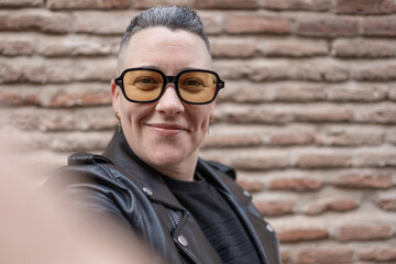 Smiling woman with yellow sunglasses taking a selfie in front of brick wall