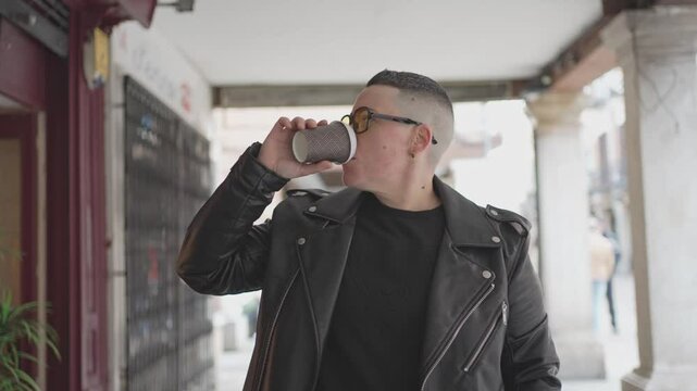 Young gender non-conforming person drinking coffee outside store