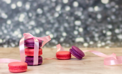 pink and purple macarons lying in a column tied with a bow on a silver background close-up