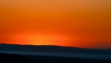 Obraz premium Fiery sunset over a silhouetted landscape. Vivid oranges and deep blues create a dramatic scene.