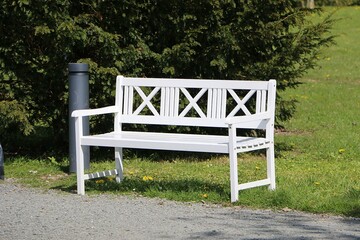 pretty white wooden bench with ornaments stands in a park and next to it a garbage can