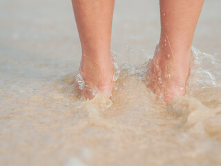 Fototapeta premium Travel alone. Barefoot standing on the sandy beach at a seaside. Both feet of a woman standing on the shore with waves of the sea. Lifestyle, travel and vacation. A person standing in the bay