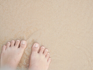Travel alone. Barefoot standing on the sandy beach at a seaside. Both feet of a woman standing on the shore with waves of the sea. Lifestyle, travel and vacation. A person standing in the bay