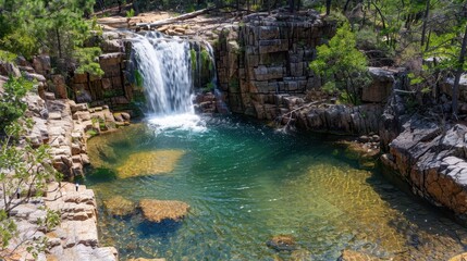 Obraz premium A serene waterfall cascading into a tranquil pool surrounded by rocky terrain and lush greenery.