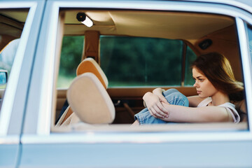 Naklejka premium Sad young woman in casual outfit sitting in the backseat of a car, expressing deep emotions and reflection amidst a blurred green background.