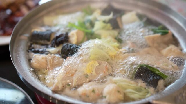closeup sukiyaki or hot pot to boiling water or suki soup bubbles steam from heat with meatball vegetable and seaweed wrapped meatballs for dinner or lunch at japanese food restaurant in thailand