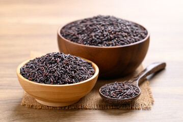 Organic rice berry or purple rice in wooden bowl with spoon on wooden background, Thai rice