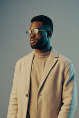 Fototapeta premium Stylish young man in a light coat and round glasses against a pastel background, exuding confidence and modernity in a seasonal fashion shoot