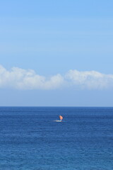 Sailboat Navigates Blue Ocean Waters with Fluffy Clouds Peacefully Drifting Across a Vibrant Sky
