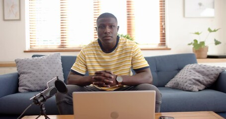 Sitting on couch, african american man with laptop and microphone, podcast recording, at home