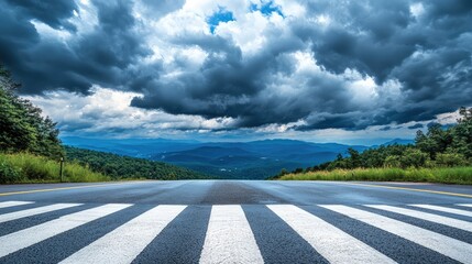 A wide-angle shot of a crosswalk leading into a mountain road, surrounded by open countryside under a dramatic cloudy sky