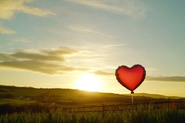 Heart-Shaped Balloon Floating at Sunrise Over a Peaceful Countryside Landscape