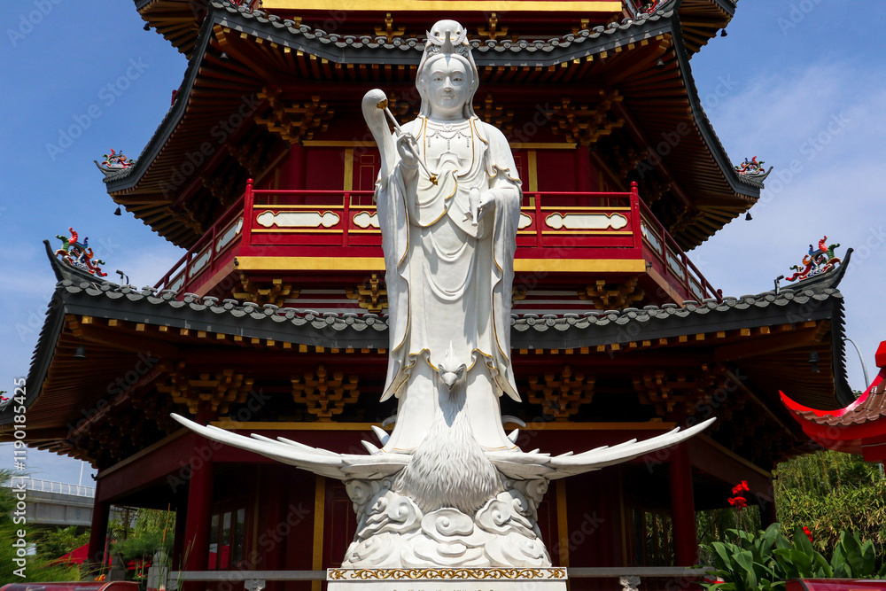 Wall mural A detailed close-up of a magnificent white Guan Yin statue, positioned in front of a vibrant red and gold Chinese pagoda.