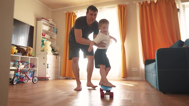Father teaches his son to skateboard. Skate skater board family dream concept. A child is learning to skateboard indoors. Father teaches his son how to skateboard indoors happy fun childhood.