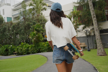 A woman is walking at the city park while carrying a skateboard in her hands