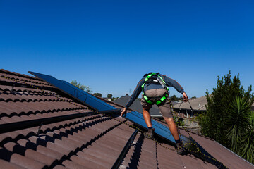 tradie climbing on house roof wearing safety harness clipped to rope installing solar power system
