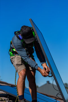 Electrician tradesman connecting bifacial solar panels together on roof during installation job
