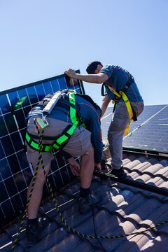 Tradesman electrician and apprentice installing solar panel system on rooftop in Australia