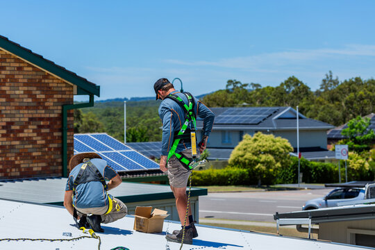 Electrician tradie worker men on roof of suburban house installing solar panel system in suburbs