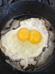 Frying double yoked egg in iron skillet in butter.
