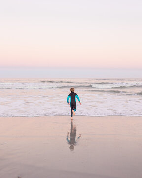 boy in wetsuit with boogie board running to the ocean