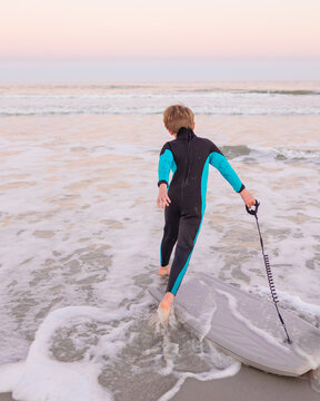 boy in wetsuit with boogie board running to the ocean