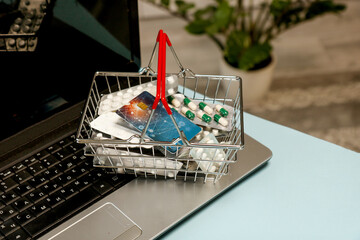 shopping basket with medicines and bank card at home next to laptop, online shopping