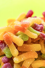 gummy worms yellow and orange in sugar sprinkles, multicolored candies on a green background