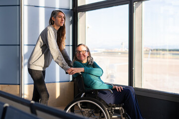 Daughter assisting her elderly mother in wheelchair at airport waiting area