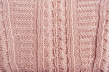 Complex knitting for advanced needlewomen: combining patterns. Woolen fabric created using several knitting techniques. A pink sweater with a pattern neatly laid out on the surface, close-up.