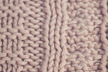 Texture of a sweater knitted using a complex technique: close-up patterns on fabric made of fluffy light pink yarn. Knitting techniques for advanced users: a sample of a finished product.