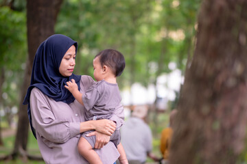 Fototapeta premium image of an asian mother and baby having fun in the park. Mother and baby playing in the park at the sunset time. Family, trust, protecting, care, parenting, summer vacation concept.