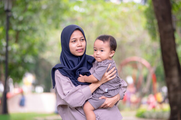 Fototapeta premium image of an asian mother and baby having fun in the park. Mother and baby playing in the park at the sunset time. Family, trust, protecting, care, parenting, summer vacation concept.