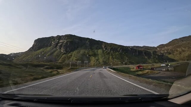 Driving through the tundra of northern Norway on E69 road. Rocky hills with grass surround the area, with the sea visible on the right side.
