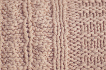 Sweater with a beautiful knitted pattern: a close-up of pale pink wool fabric photographed from above with different knitting techniques. Interlacing of vertical and horizontal rows in knitting.