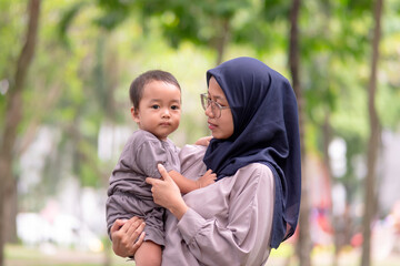 Fototapeta premium image of an asian mother and baby having fun in the park. Mother and baby playing in the park at the sunset time. Family, trust, protecting, care, parenting, summer vacation concept.