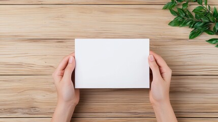 Fototapeta premium Funeral symbolic. A person holding a blank card on a wooden table with greenery nearby.