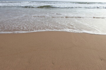waves crashing on shore of sandy beach on a cloudy day