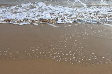 waves crashing on shore of sandy beach on a cloudy day