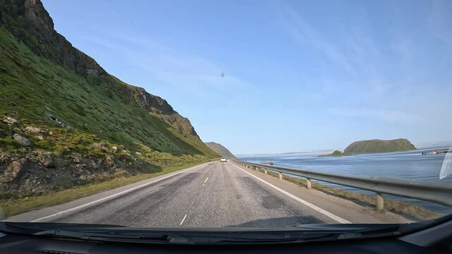 Driving through the tundra of northern Norway on E69 road. Rocky hills with grass surround the area, with the sea visible on the right side.
