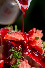 A vibrant and refreshing dessert featuring a slice of creamy cheesecake topped with fresh strawberries and a drizzle of sweet berry sauce.