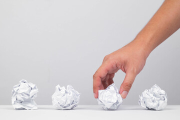 A hand picking up a crumpled paper amidst several others on a table, symbolizing ideas or creative...
