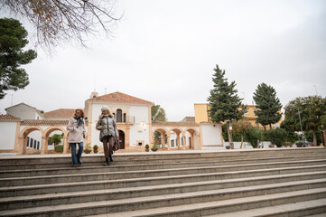 Two women descending stone stairs near a historical building in a Spanish town, enjoying a cultural...