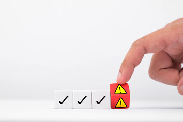 A hand presses a warning block among marked checkboxes, symbolizing caution and evaluation in decision making.