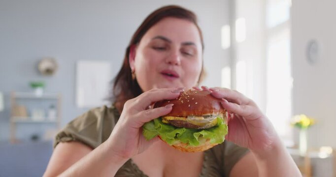 Obese hungry happy woman with excessive fat eating unhealthy fast food, tasty hamburger, juicy burger, cheeseburger, chubby overweight plus size big fat fit lady with good appetite, excess calories 