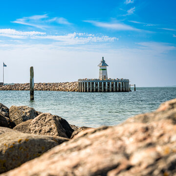 Blick auf das Signallicht West Mole Head light in der Hafeneinfahrt von Ebeltoft, im Vordergrund unscharf Steine der K&uuml;stenlinie, 1:1-Format