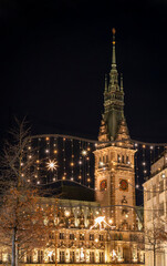 Fototapeta premium Blick auf den Turm des beleuchteten Rathauses in Hamburg während der Weihnachtszeit, Weihnachtslichter im Vordergrund, vertikal